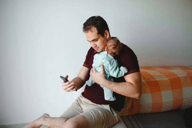 padre que mira el móvil con un bebé en brazos