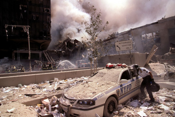 1074px-Rescue_worker_reaching_into_a_New_York_Police_car_covered_with_debris_(28802606564)