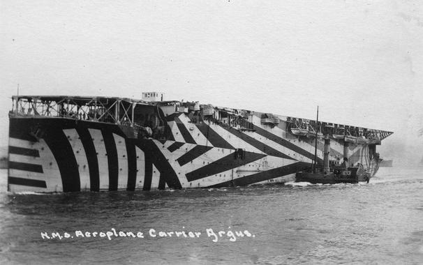 <p>No solo era cuestión de camuflar a las personas, también era necesario ocultar a los objetos, aunque fuesen tan grandes como un portaaviones. En de la imagen –el británico HMS Argus– aparece pintado en camuflaje dazzle, una técnica pictórica aplicada desde los diseños cubistas –el arte del momento– para romper las líneas de los barcos en el mar. / National World War I Museum</p>