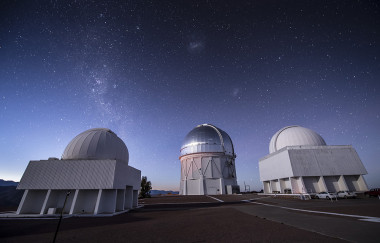 <p>Telescopio Blanco, situado en el observatorio de Cerro Tololo, en los andes chilenos. El telescopio se encuentra bajo la cúpula metálica del centro de la imagen. Sobre esta cúpula son visibles las nubes de Magallanes, dos galaxias enanas satélites de la Vía Láctea. / DES Collaboration y Fermilab.</p>