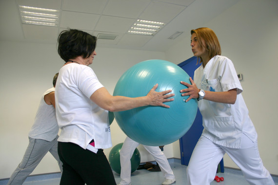 <p>Una mujer realiza ejercicios con un balón medicinal, ayudada por una terapeuta. /H. San Juan de Dios</p>