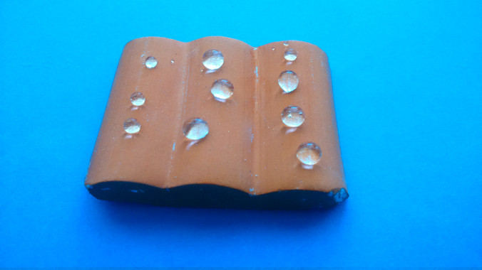 <p>Teja tras ser tratada con el material superhidrofugante. Las gotas tienen una forma totalmente esférica, con lo que se reduce el área de contacto entre el agua y la teja, permitiendo que las gotas rueden / Fundación Descubre</p>