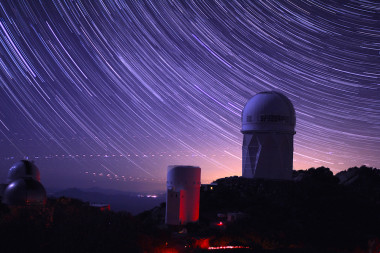 <p>Imagen de larga exposición con las trayectorias de las estrellas en el observatorio de Kitt Peak. La mayor de las cúpulas es la que aloja el telescopio de Mayall, donde se instalará DESI. / P. Marenfeld and NOAO/AURA/NSF. © 2010 The Regents of the University of California, through the Lawrence Berkeley National Laboratory.</p>